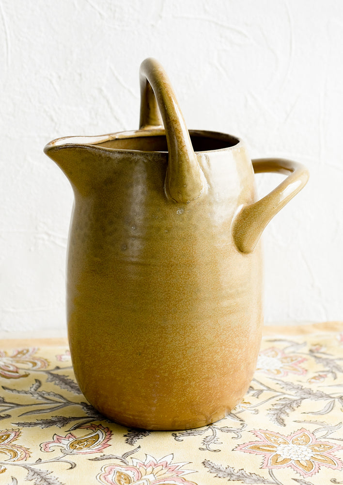 A brown ceramic pitcher with handle at top and side.