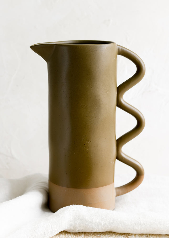 A ceramic pitcher with wavy handle dipped in olive green glaze.