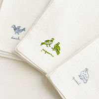 Antique Blue / Quail: White linen napkins with bird embroidery detailing.