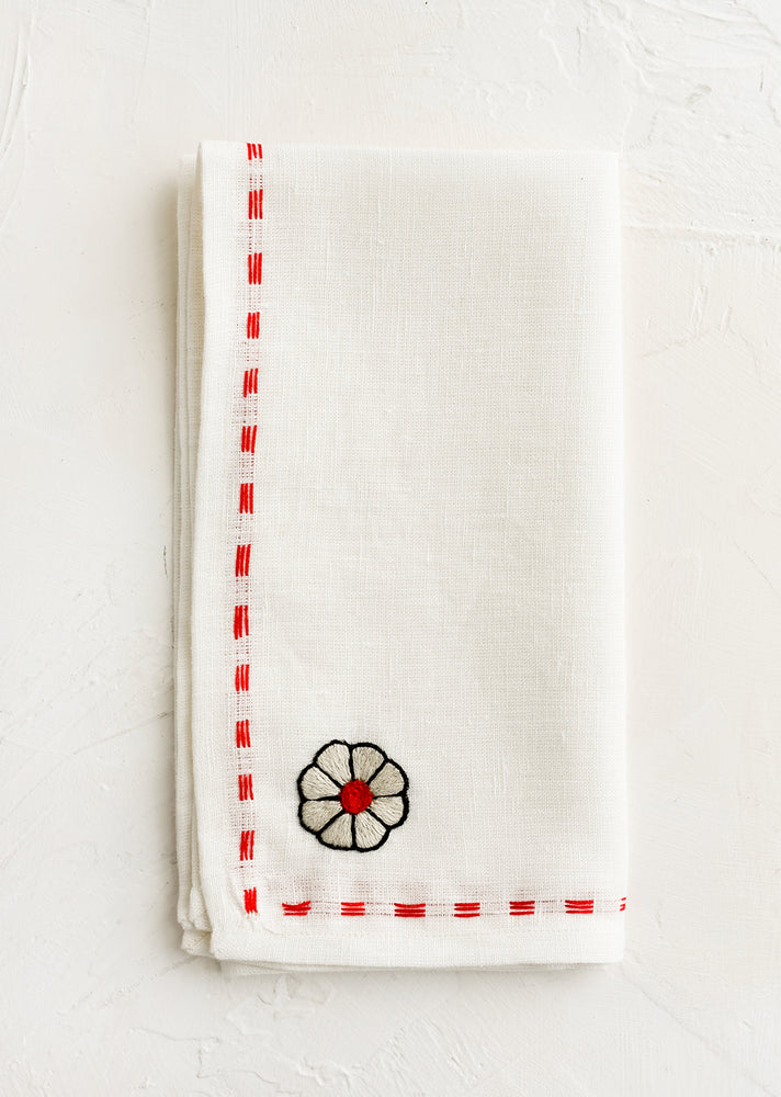 1: A white linen napkin with embroidery detailing in red.