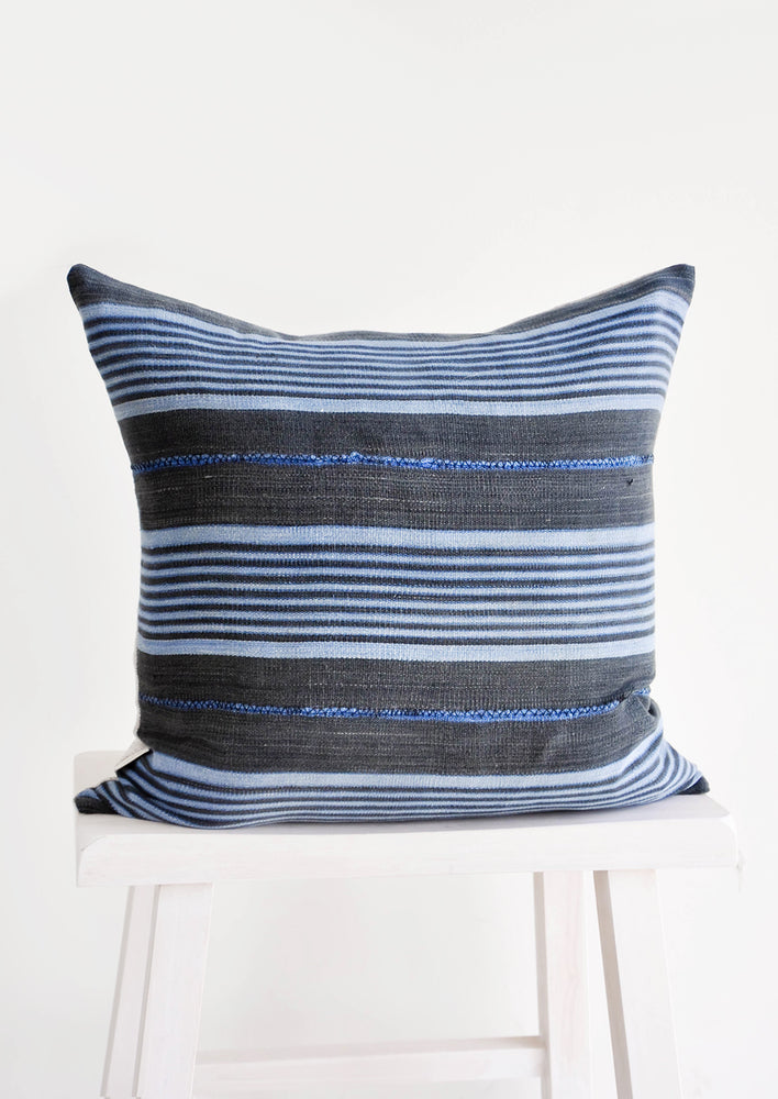 Square throw pillow in charcoal fabric with blue stripes throughout