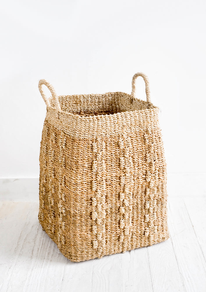 Tall, tan colored square storage basket made from banana leaf fiber with decorative woven pattern.