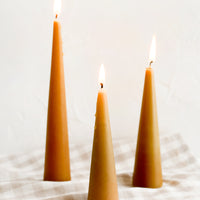 Small / Caramel: Three lit cone-shaped taper candles in caramel.