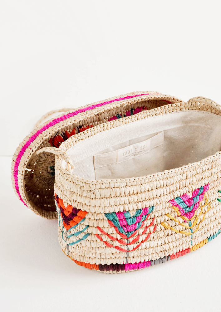2: Rounded box style straw bag with neon multicolored flower pattern shown with lid off exposing cotton interior lining.