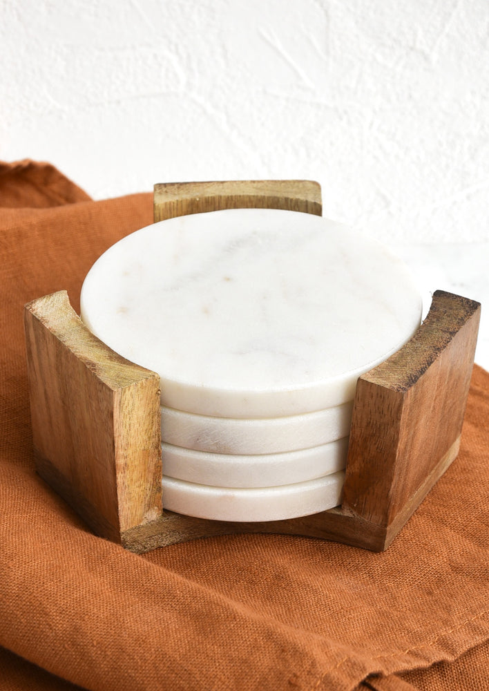 Set of four round, white marble coasters inside wooden stand