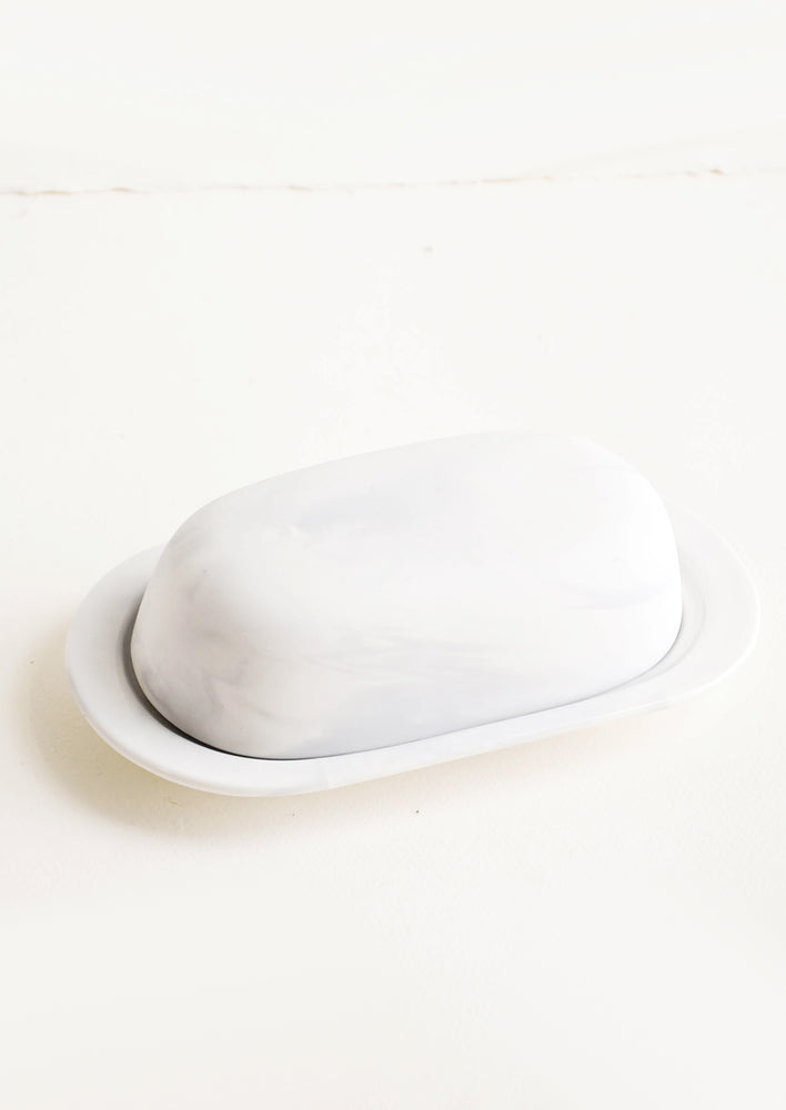 Oval shaped butter dish with curved dome lid, matte white ceramic with pale grey marbleized effect 