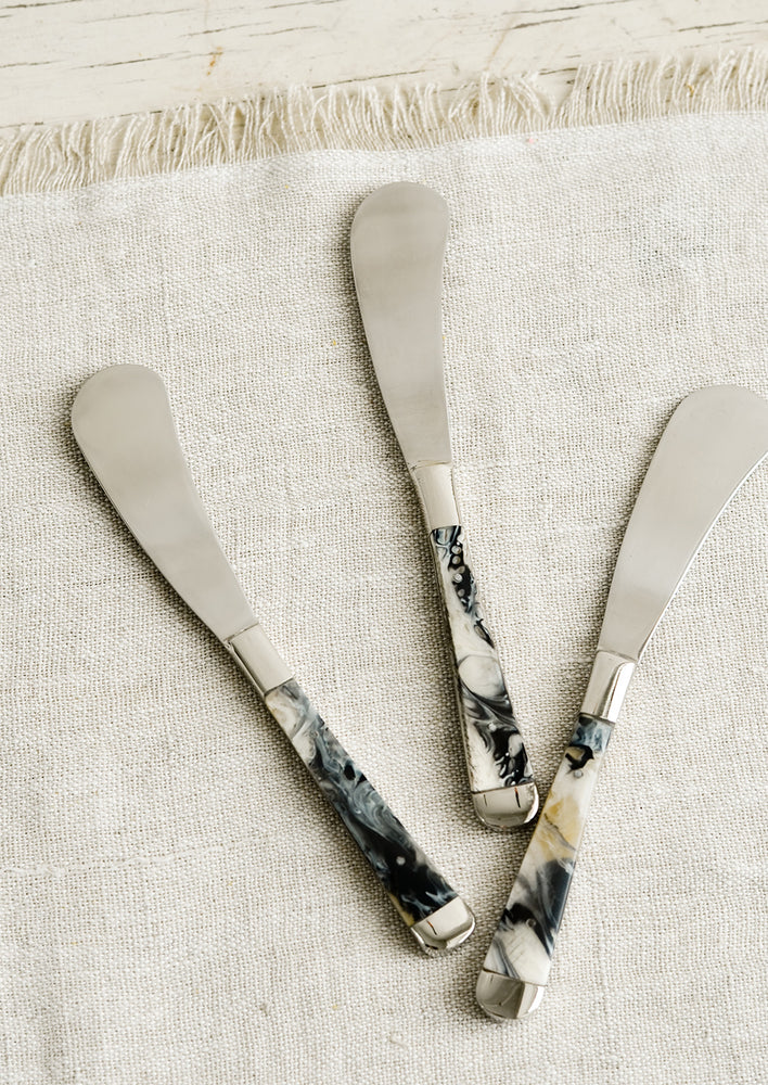 Stainless steel canape knives with marbled horn handles resting on natural linen.