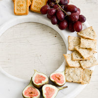 2: A circular white marble tray covered in crackers, grapes & figs.