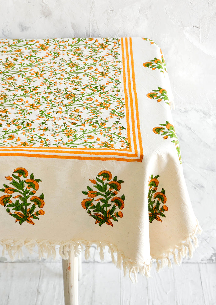 Block printed cotton tablecloth with orange and green floral pattern and tasseled edges, displayed on a table