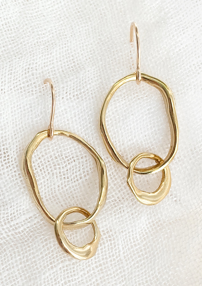 A pair of brass earrings with interconnected larger and smaller organic looking oval shapes.