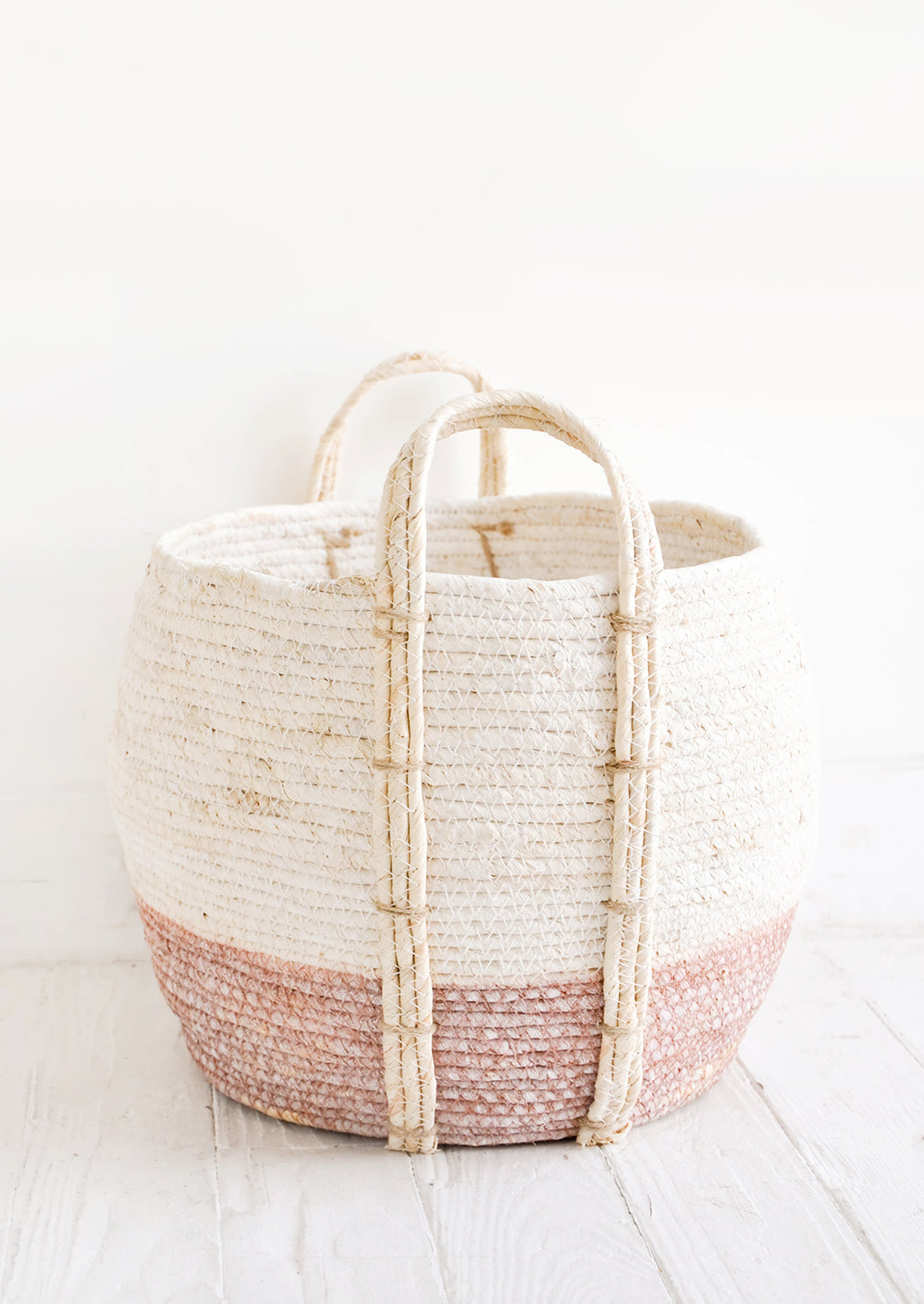 Dusty Rose / Low [Large]: Round storage basket made from natural maize fiber, fiber handles attached at sides, band of contrasting pink color along bottom.