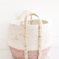 Dusty Rose / Low [Large]: Round storage basket made from natural maize fiber, fiber handles attached at sides, band of contrasting pink color along bottom.