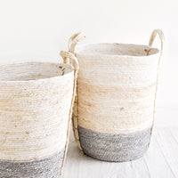 Slate / Tall [Small]: Tall, round storage baskets made from natural maize fiber, fiber handles attached at sides, band of contrasting grey color along bottom.