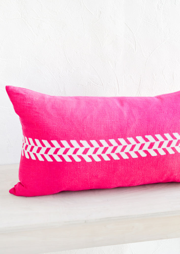 A lumbar throw pillow in bright pink linen with white herringbone block print detail across middle.
