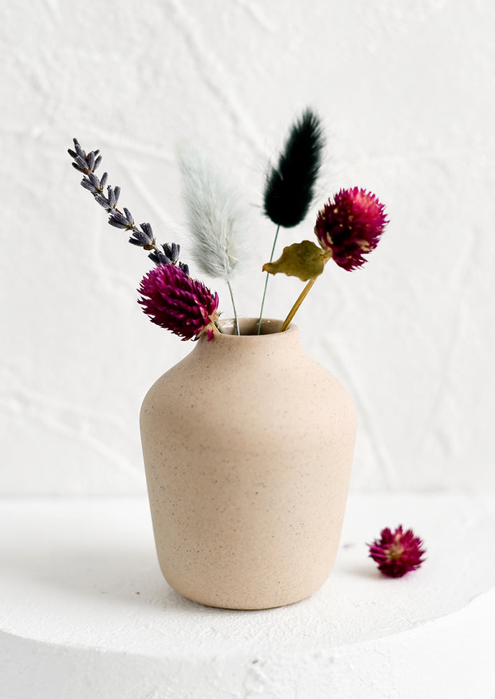 3: A sand colored porcelain bud vase with dried flowers.