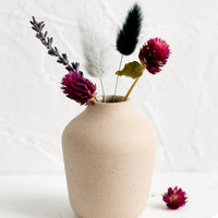 3: A sand colored porcelain bud vase with dried flowers.