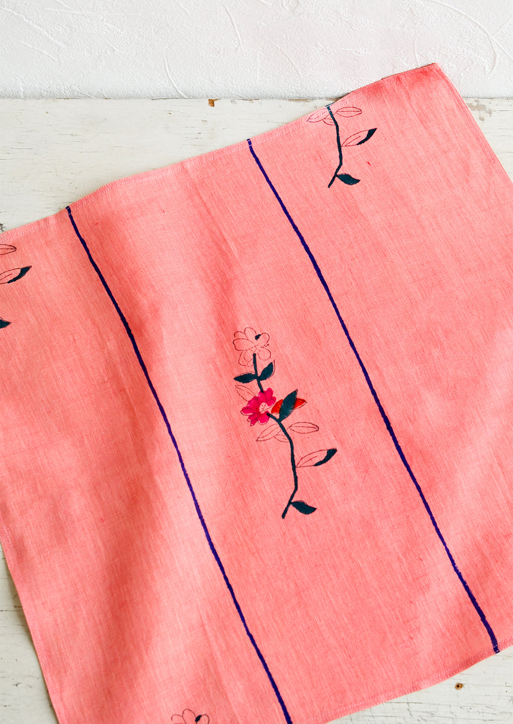 2: A pink linen napkin with a minimal floral block print design and two vertical blue stripes.