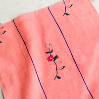 2: A pink linen napkin with a minimal floral block print design and two vertical blue stripes.