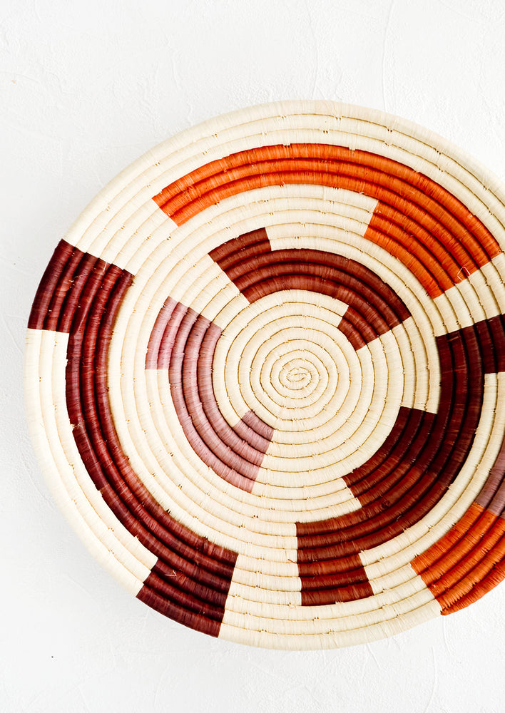 1: Round woven raffia bowl with interlocking, maze-like pattern in mauve, wine and orange