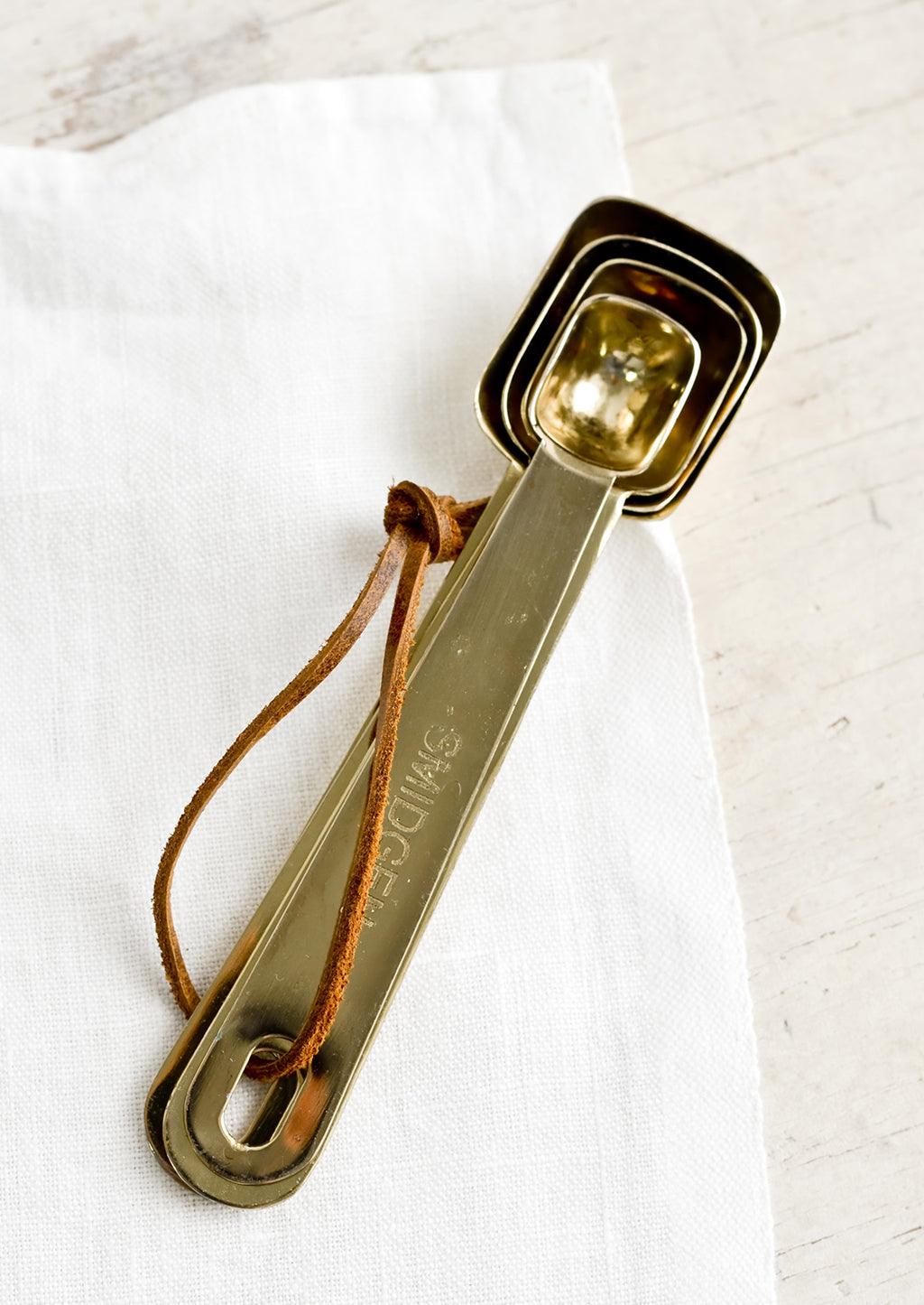 2: A set of four golden measuring spoons with brown leather tie.