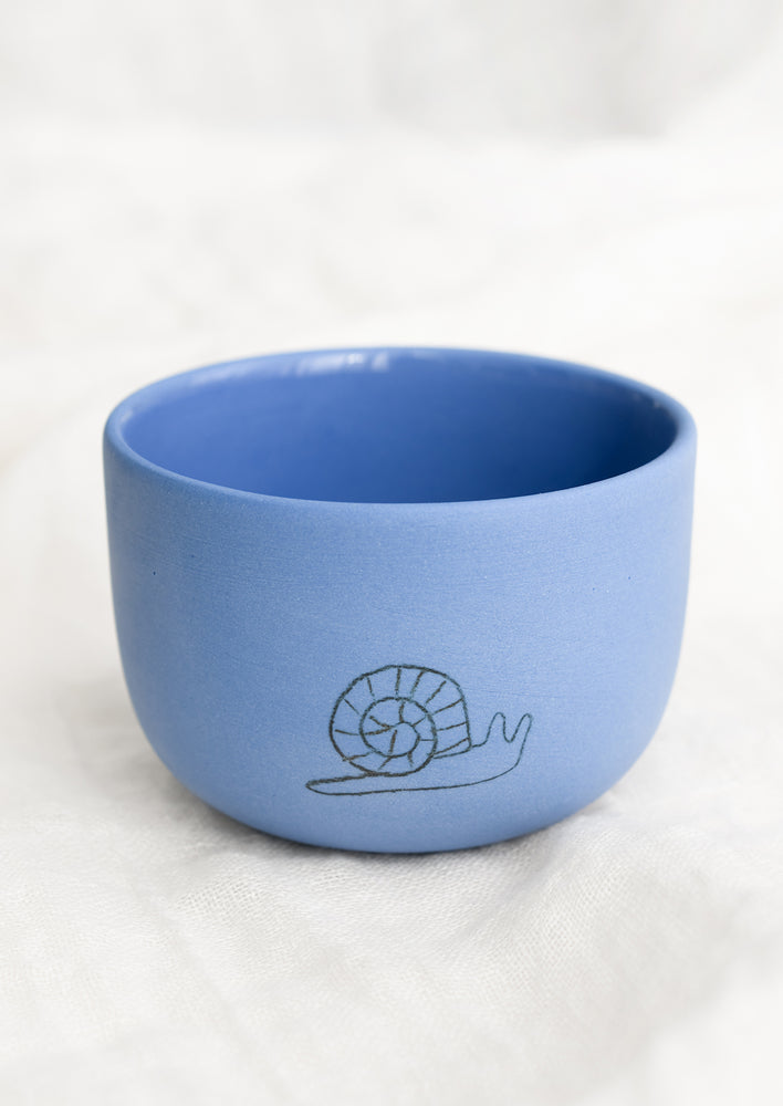 A short and wide cornflower blue cup with snail sketch.