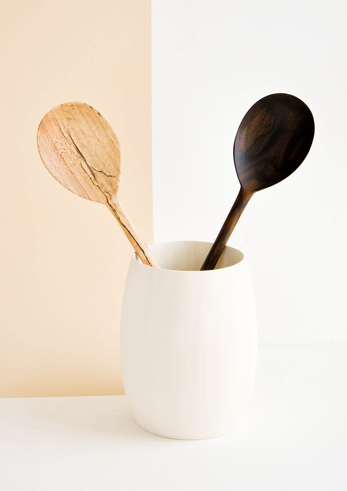 Two wooden spoons displayed in a very pale wooden vase-like container.