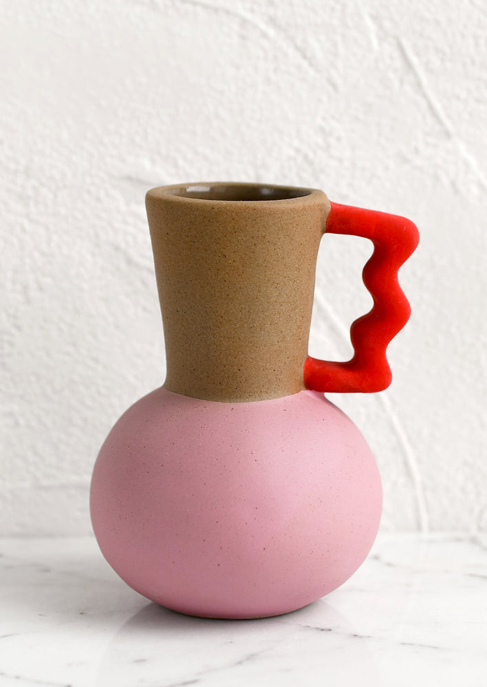 A small ceramic bud vase in pink and brown with squiggly red handle.