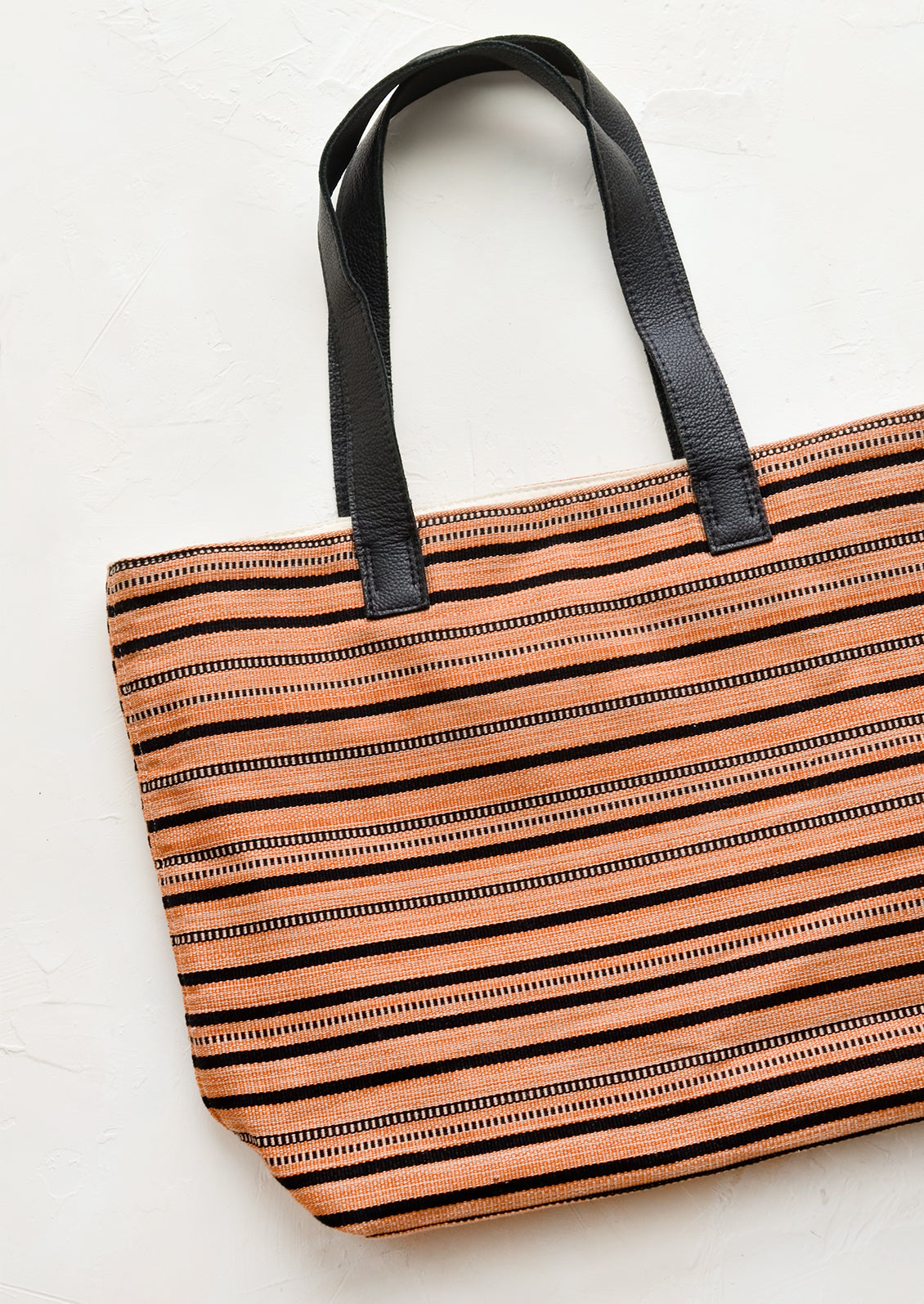 A striped canvas tote bag with black leather handles.
