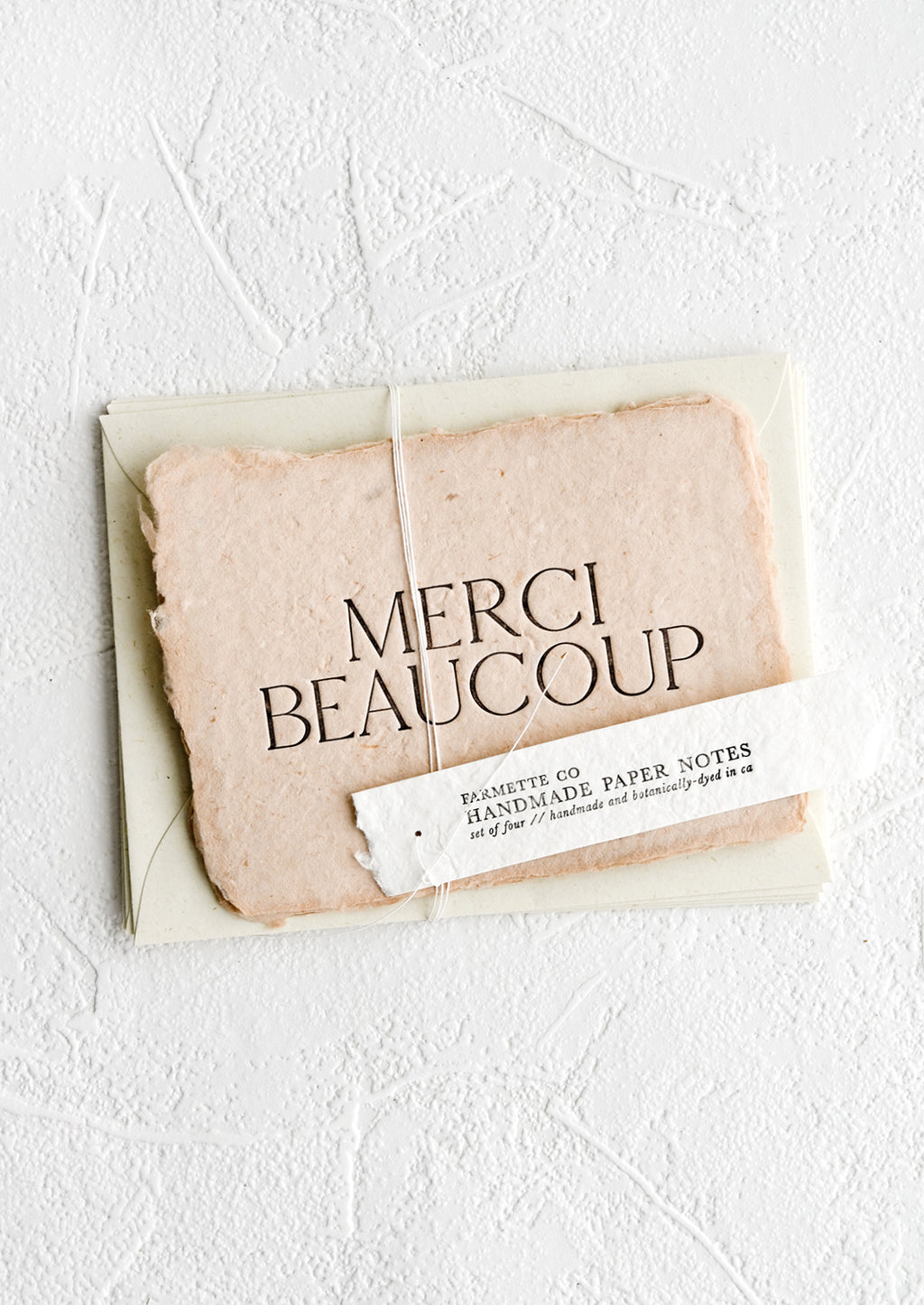Set of 4: A pack of greeting cards made from blush handmade paper and large letters spelling "Merci Beaucoup".