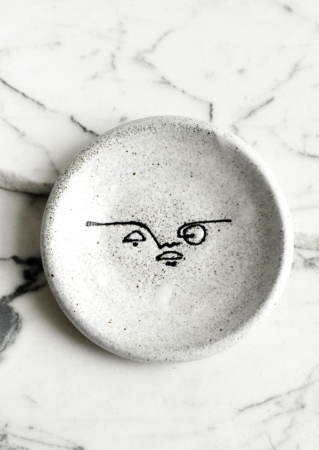 Monochrome: A small speckled ceramic trinket dish with and painted expressionist faces.