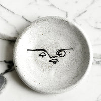 Monochrome: A small speckled ceramic trinket dish with and painted expressionist faces.