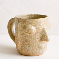 Natural: A clay mug in speckled sand color in face shape.