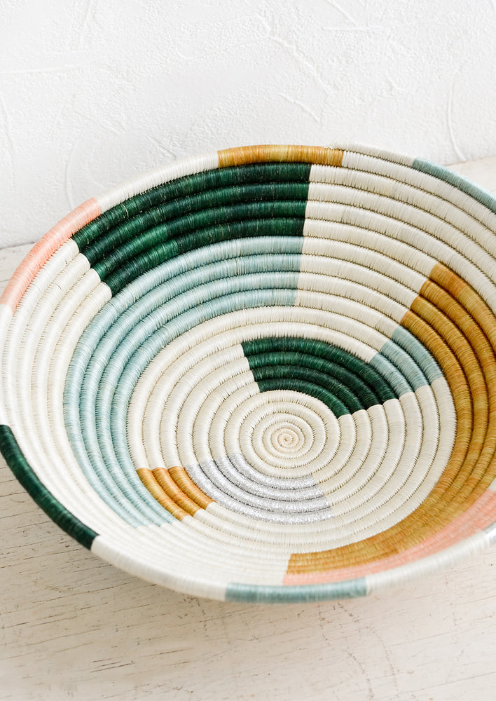 A round bowl made from woven sweetgrass in white, multiple pastels and silver.