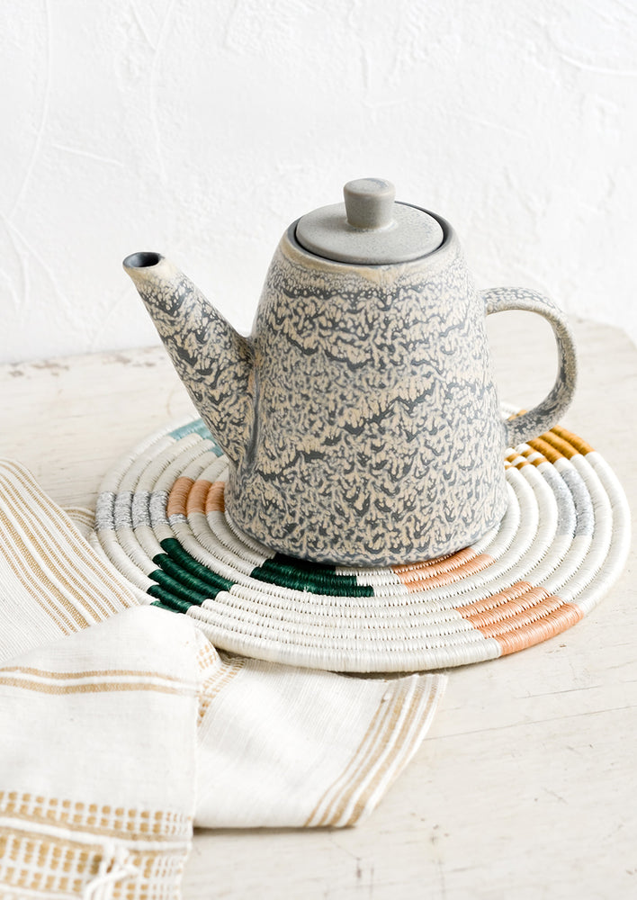 A ceramic teapot and white trivet on a table.