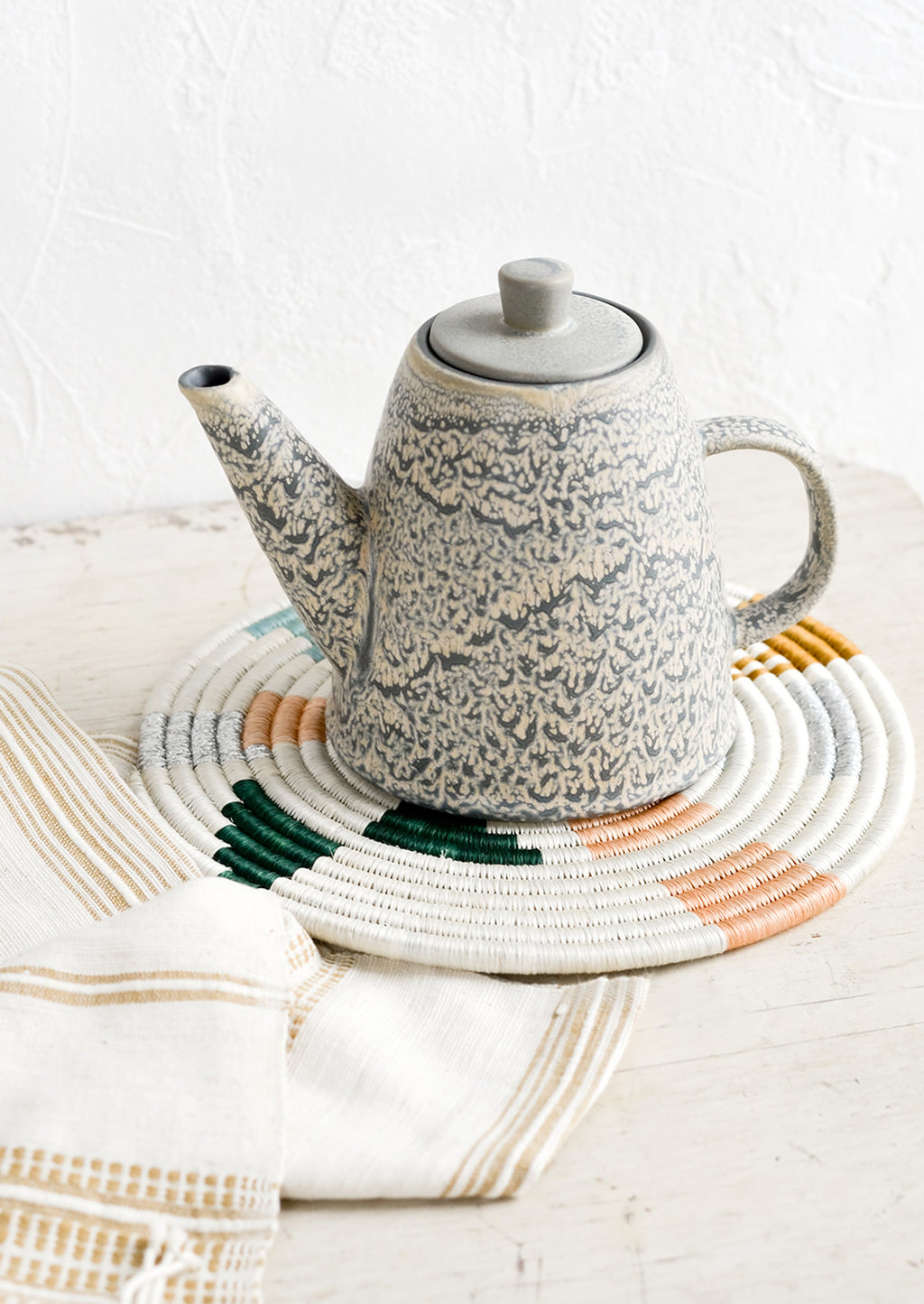 2: A ceramic teapot and white trivet on a table.