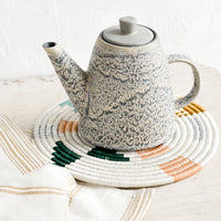 2: A ceramic teapot and white trivet on a table.
