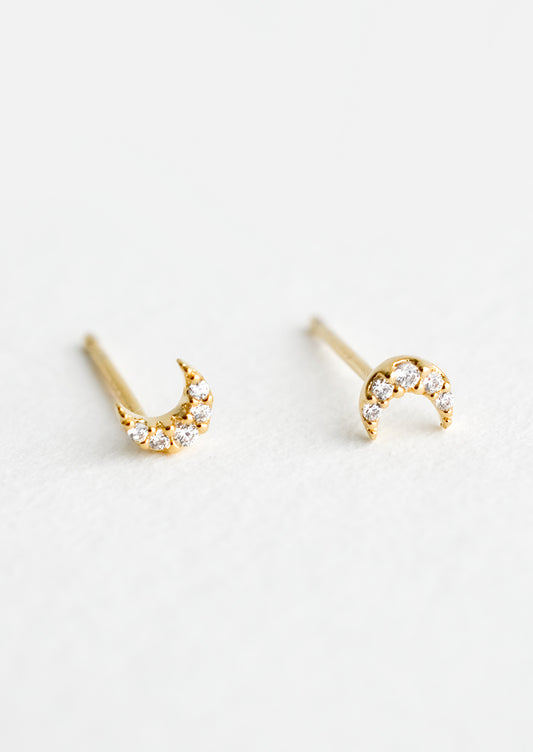 A pair of very tiny gold stud earrings in the shape of crescent moons, covered in clear crystals.