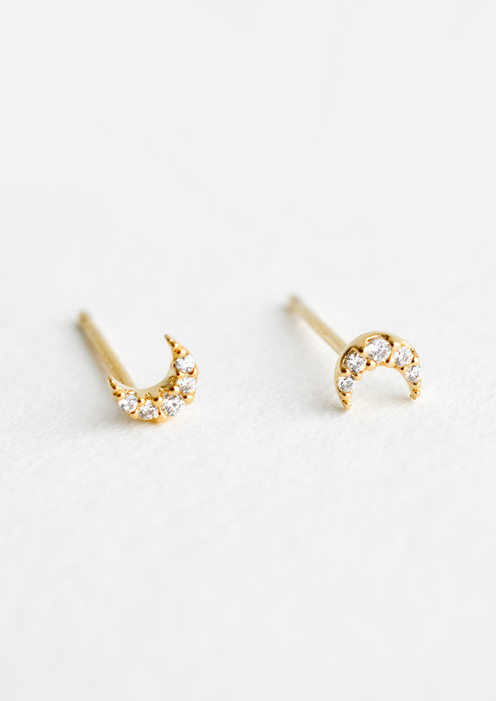 1: A pair of very tiny gold stud earrings in the shape of crescent moons, covered in clear crystals.