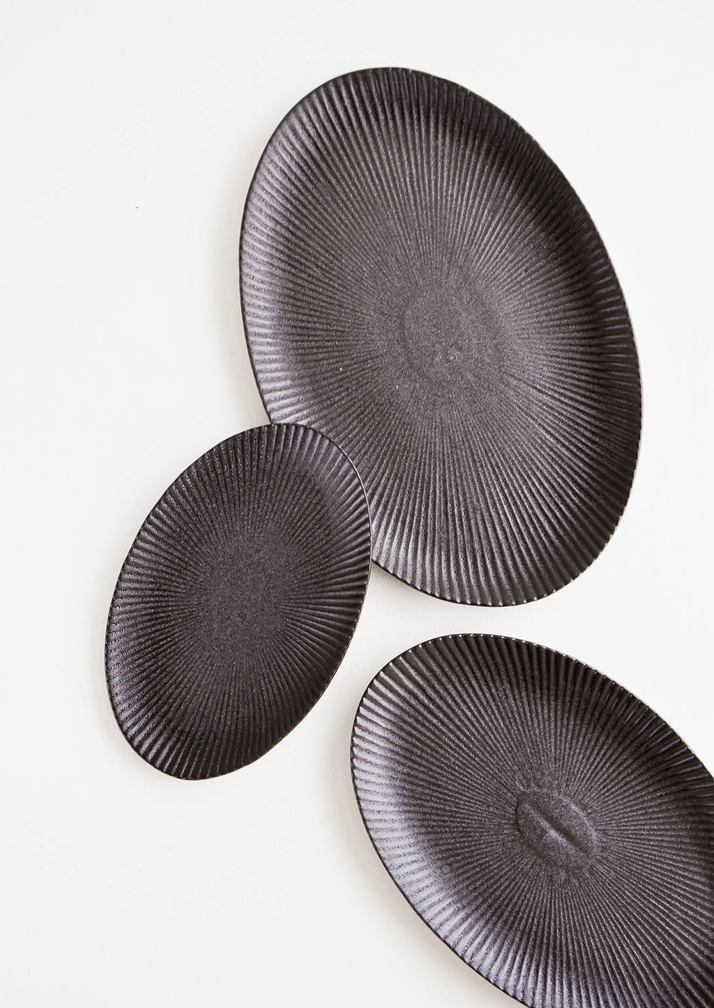 1: Oval-shaped, black ceramic trays with radiating lines pattern in a mix of incremental sizes
