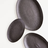 1: Oval-shaped, black ceramic trays with radiating lines pattern in a mix of incremental sizes