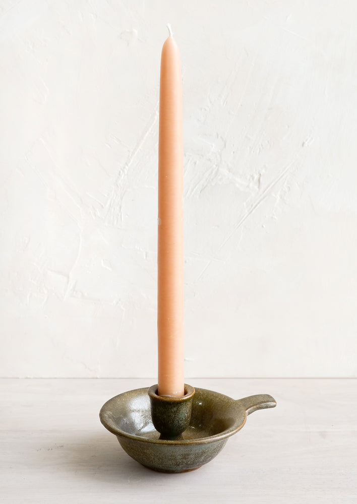 A ceramic taper holder in old fashioned silhouette holding taper candle.