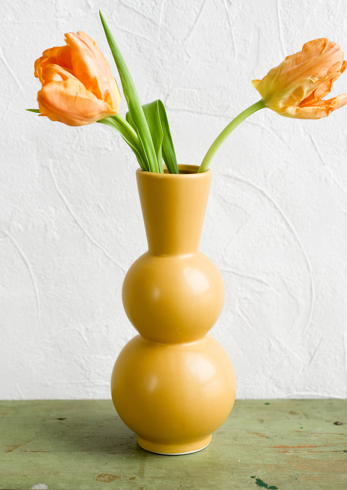 A yellow ceramic vase with orange tulips.