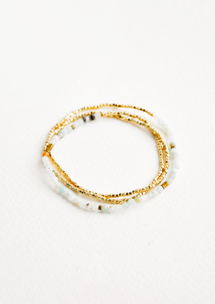 A single strand bracelet of gold and play green stone beads wrapped upon itself in three layers. 