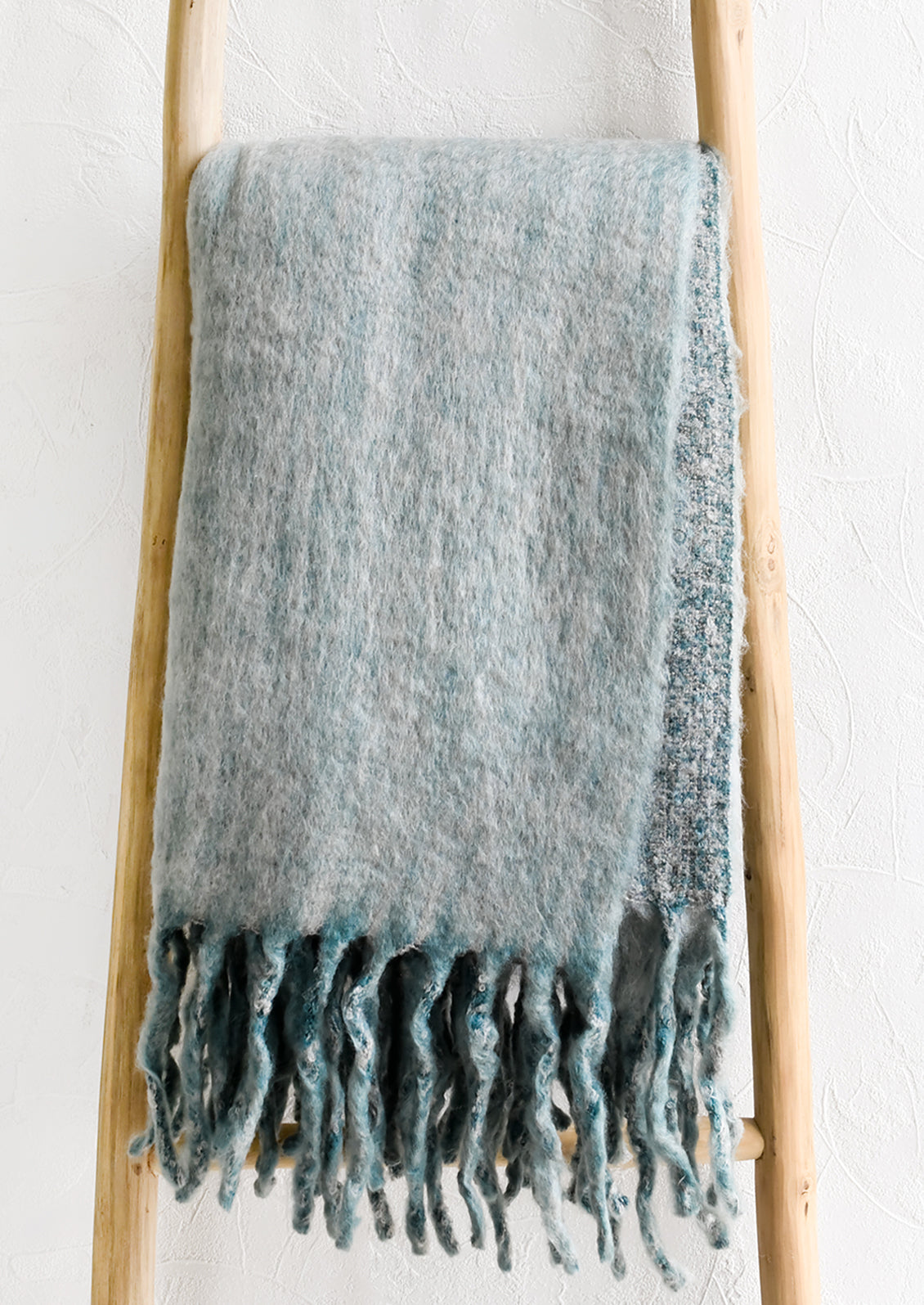 A blue-grey mohair throw blanket displayed on a ladder.