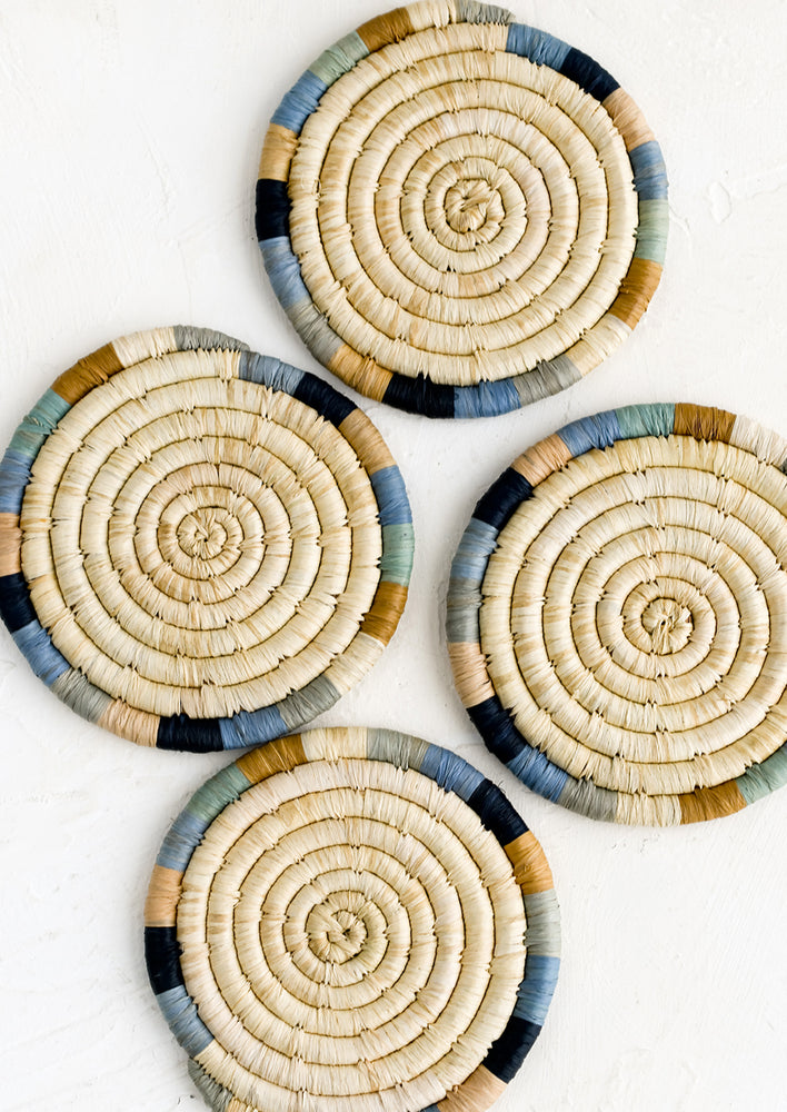 A set of four round coasters in natural raffia with blue colorblock border.