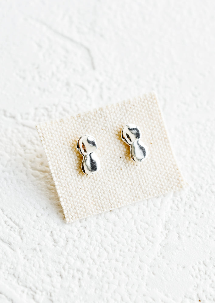 A pair of silver stud earrings on canvas card featuring a drippy, melty appearance.