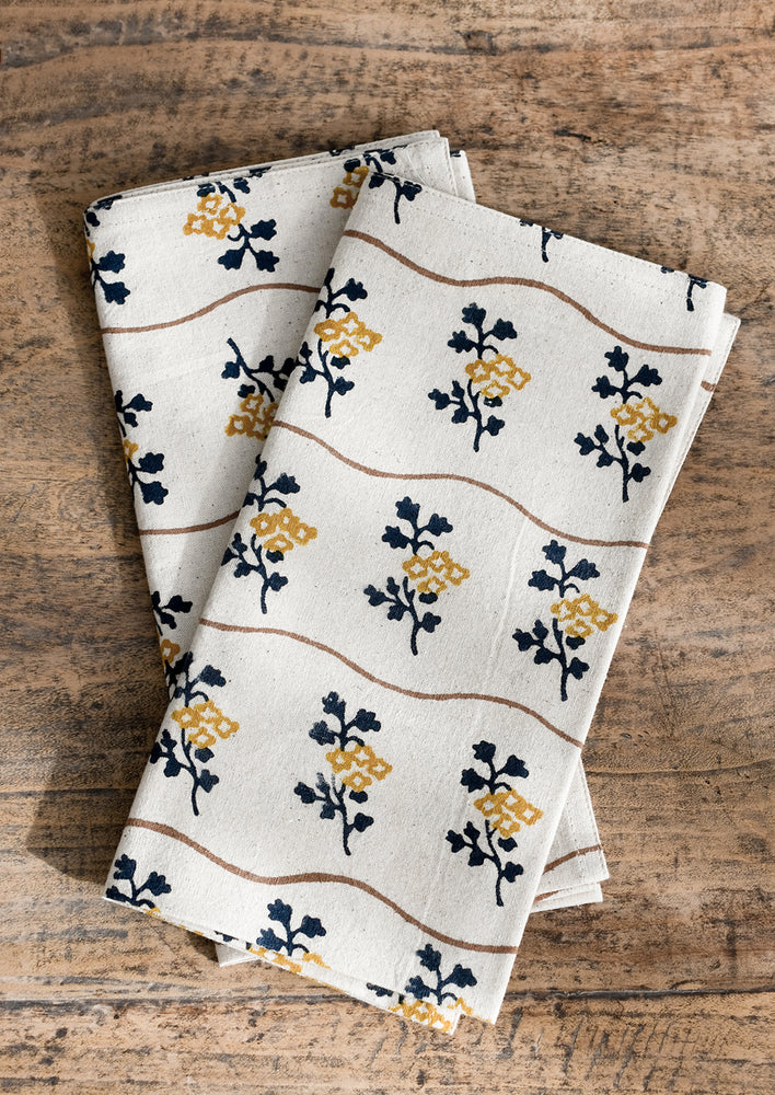 2: A natural cotton napkin with wavy brown line and navy/mustard flower print.