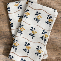 2: A natural cotton napkin with wavy brown line and navy/mustard flower print.