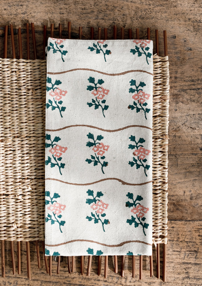 A natural cotton napkin with wavy brown line and green/peach flower print.