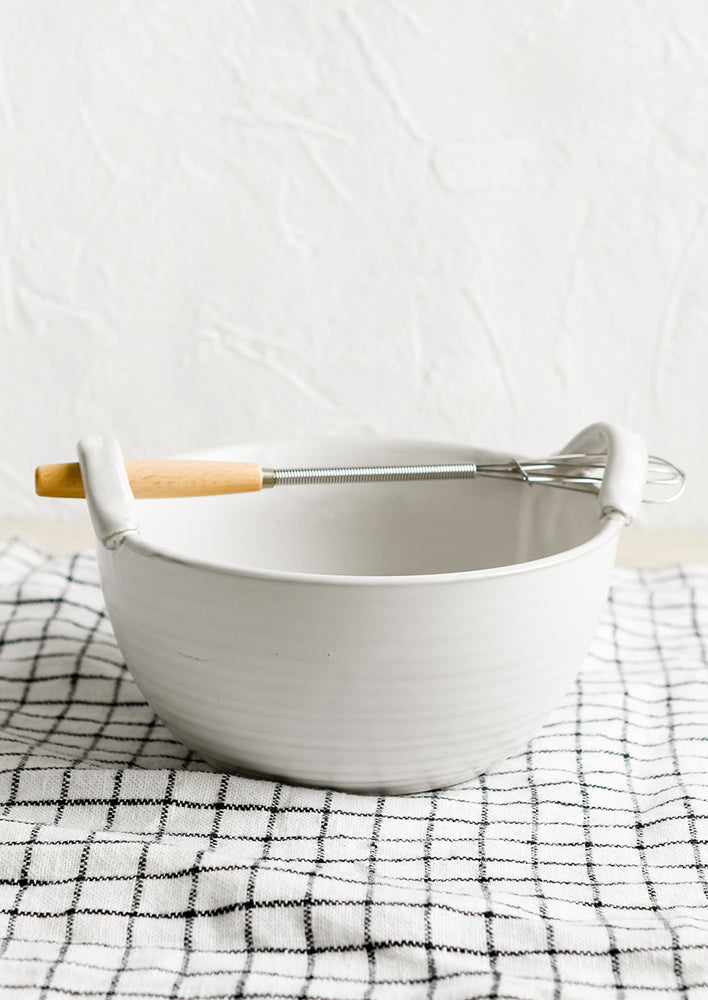 A white ceramic bowl with top handles that fit included whisk.